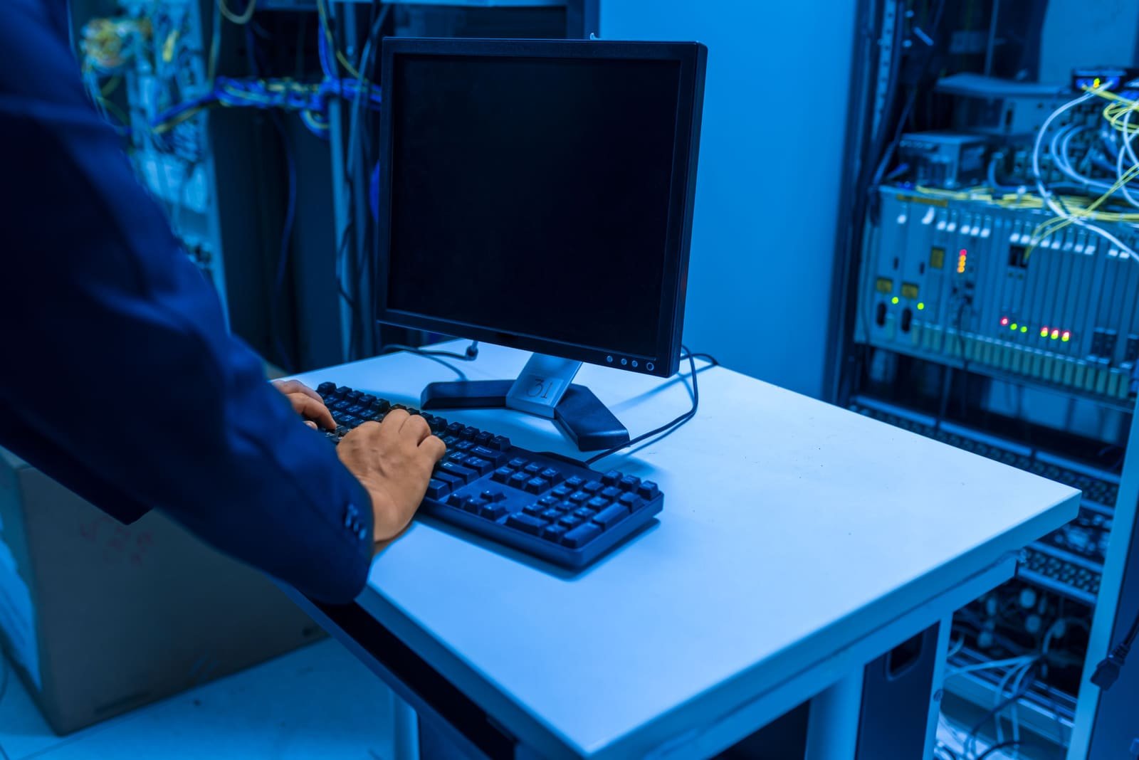 Un administrateur au clavier d'une console dans une salle serveurs baignée de bleu