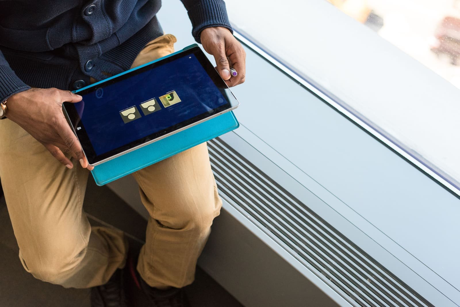 Un homme assis près d'une fenêtre consultant une tablette tactile